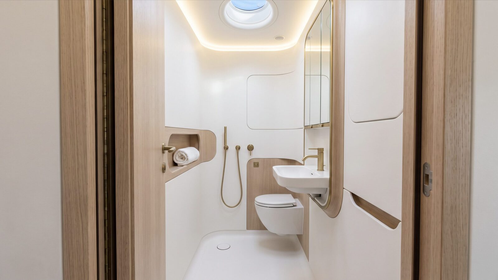 A compact white lavatory with oak trim and a brass shower